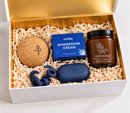 Holiday Wellness &amp; Tech gift box with sleep earbuds, UV sanitizing case, magnesium cream, cork massage ball, and sandalwood candle in a white and gold box
