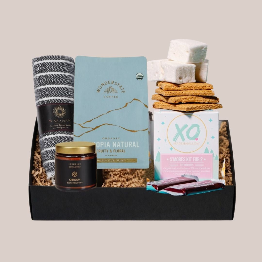 Hug in a Box gift set with woven blanket, coffee, candle, and s’mores kit arranged in a black gift box